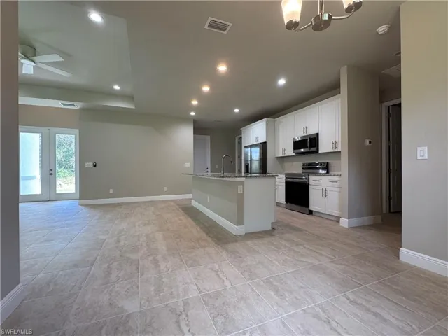Kitchen with white cabinets, a center island with sink, appliances with stainless steel finishes, ceiling fan with notable chandelier, and sink