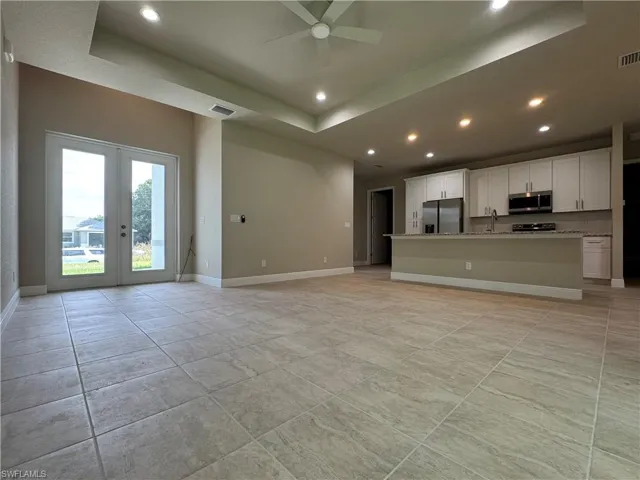 Unfurnished living room featuring sink, french doors, a tray ceiling, and ceiling fan