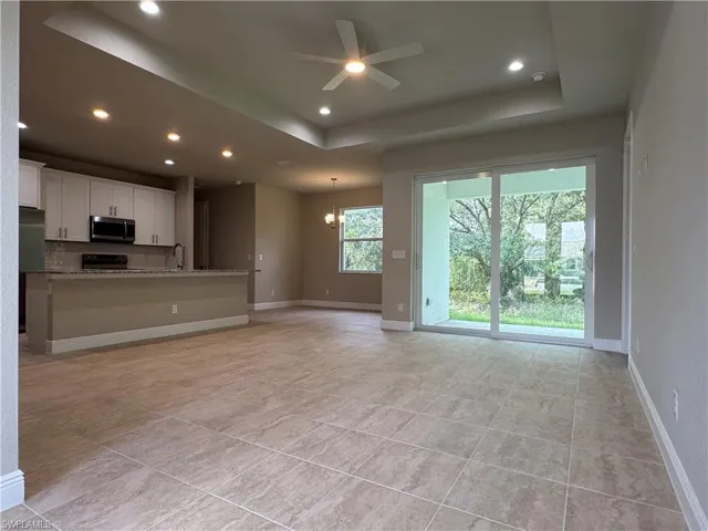 Unfurnished living room featuring sink, a tray ceiling, ceiling fan with notable chandelier, and light tile patterned floors
