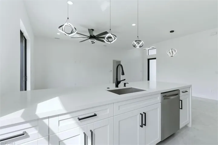 Kitchen featuring light stone counters, white cabinetry, pendant lighting, a ceiling fan, and stainless steel dishwasher