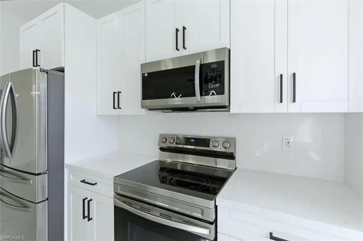 Kitchen featuring stainless steel appliances, light stone countertops, and white cabinetry