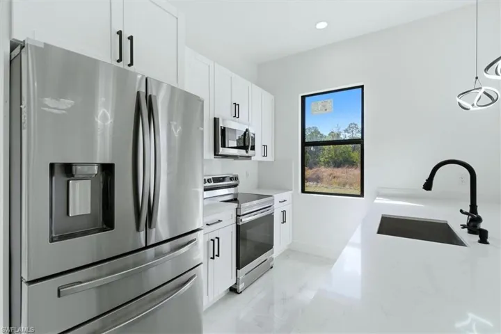 Kitchen featuring stainless steel appliances, light stone counters, white cabinetry, and hanging light fixtures