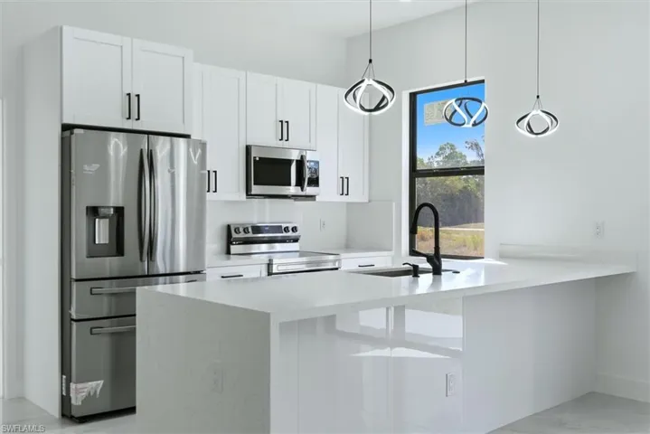 Kitchen with stainless steel appliances, a peninsula, white cabinetry, and light stone counters