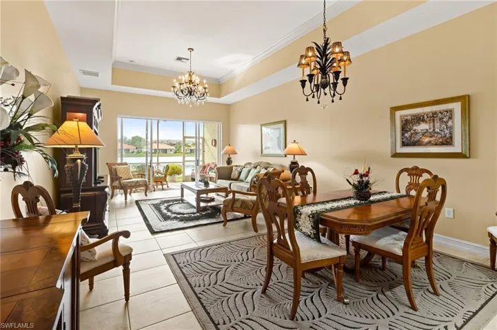 Living room with light tile patterned flooring, a tray ceiling, a chandelier, ornamental molding, and a residential view
