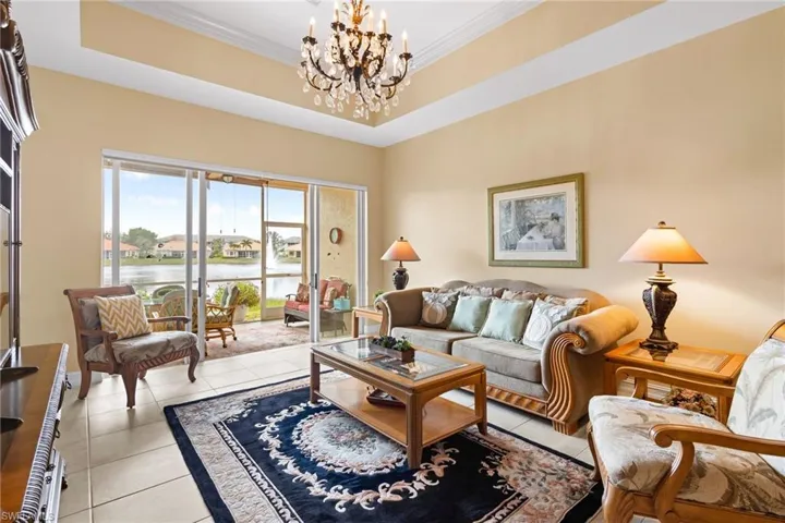 Living room with a water view, light tile patterned flooring, a chandelier, a raised ceiling, and crown molding