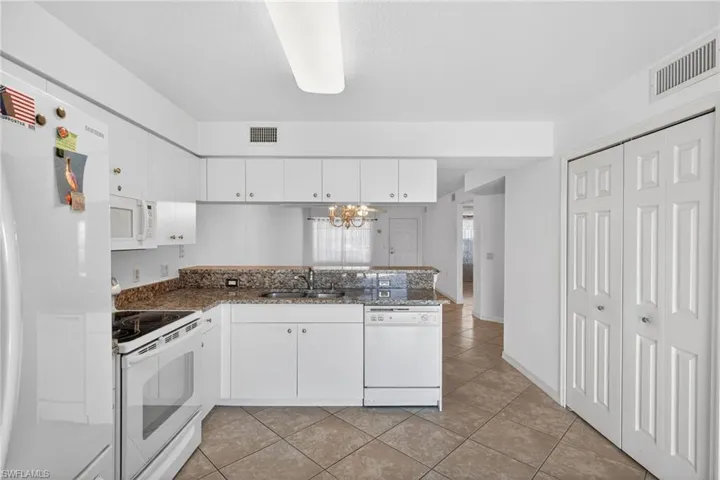 Kitchen featuring white appliances, white cabinetry, a peninsula, hanging lights, and light tile patterned floors