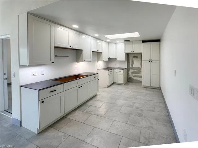 Kitchen with dark countertops, a skylight, white cabinetry, and recessed lighting