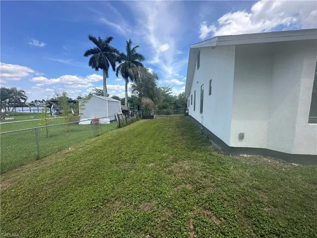 Expansive green space featuring a chain-link fence, a white storage shed, and mature palm trees