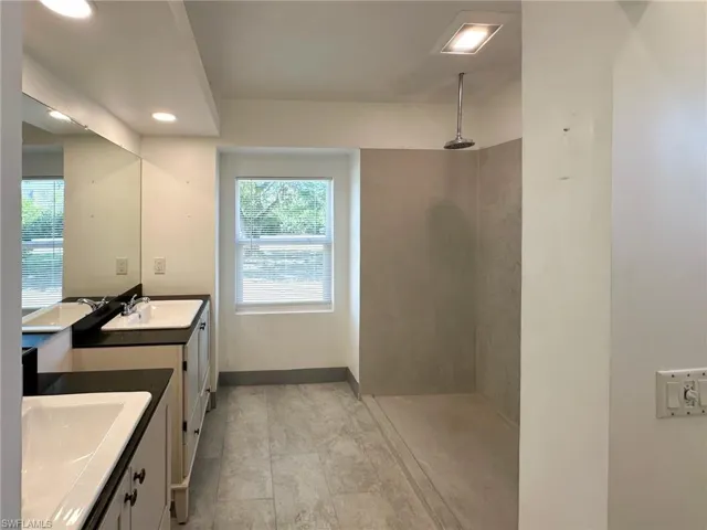 Full bathroom featuring a walk in shower, two vanities, and recessed lighting