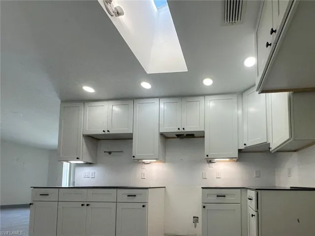 Kitchen featuring white cabinets, a skylight, under cabinet range hood, and dark countertops