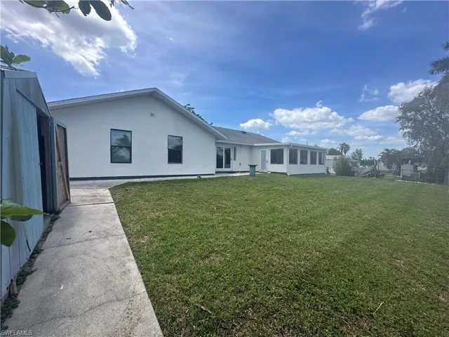 Spacious green lawn with a white stucco exterior home, featuring dark-framed windows and a screened enclosure