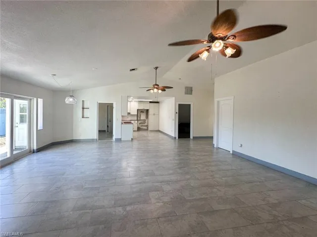 Unfurnished living room with lofted ceiling, ceiling fan, and a textured ceiling