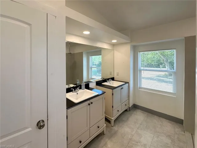 Bathroom featuring vaulted ceiling, two vanities, healthy amount of natural light, and recessed lighting
