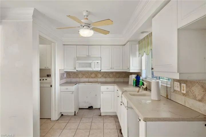 Kitchen with light tile patterned floors, ornamental molding, sink, white cabinetry, and ceiling fan