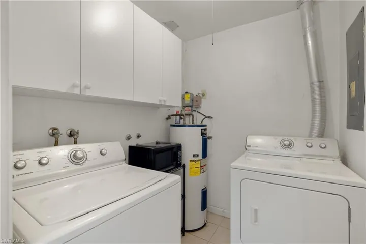 Clothes washing area with electric water heater, light tile patterned floors, cabinets, and washer and dryer