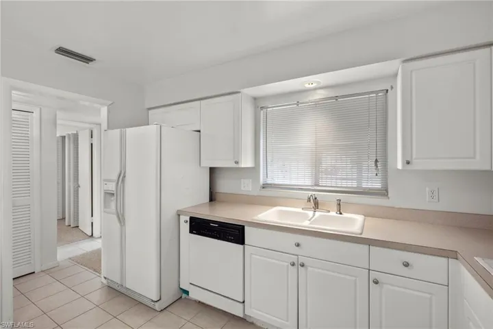 Kitchen featuring white cabinets, white appliances, light tile patterned floors, and sink