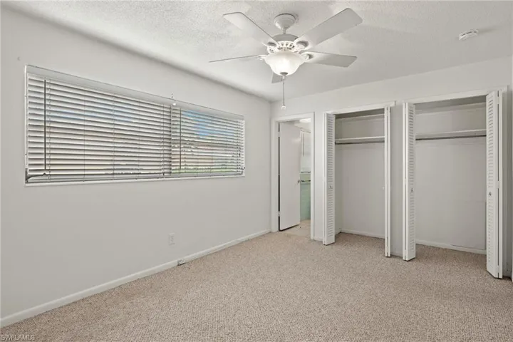 Unfurnished bedroom featuring light carpet, a textured ceiling, and two closets