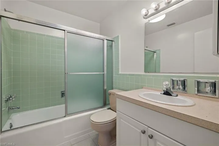 Full bathroom with toilet, tile patterned floors, vanity, tasteful backsplash, and enclosed tub / shower combo