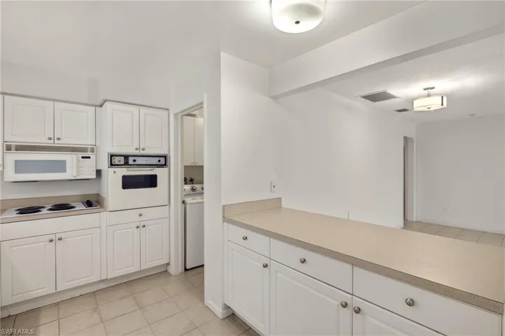 Kitchen featuring washer / dryer, white appliances, white cabinetry, and light tile patterned flooring