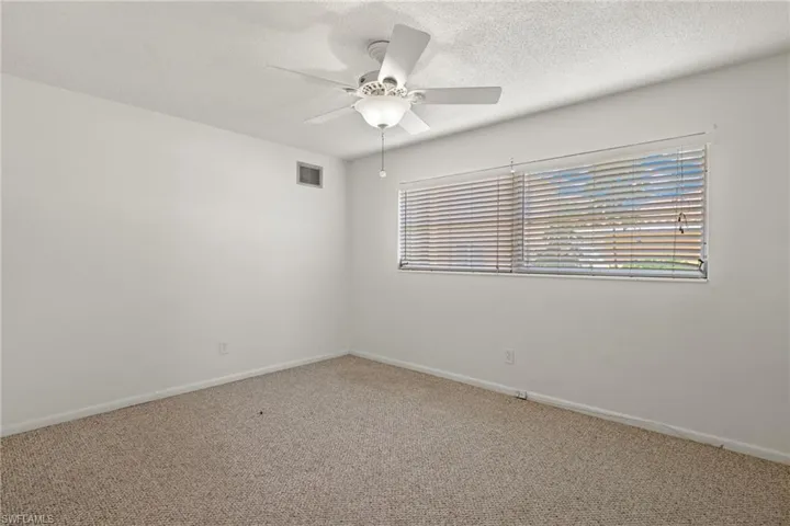Carpeted empty room with a textured ceiling, a wealth of natural light, and ceiling fan