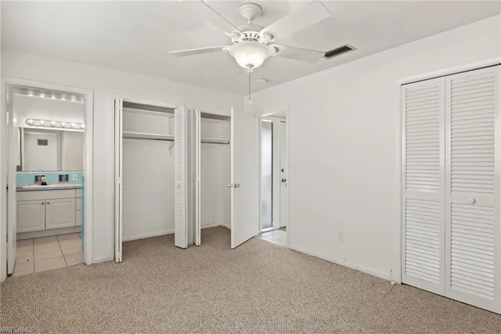 Unfurnished bedroom featuring two closets, ceiling fan, connected bathroom, and light carpet
