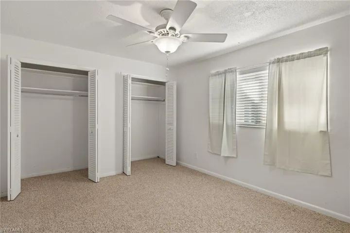 Unfurnished bedroom featuring light colored carpet, two closets, and ceiling fan