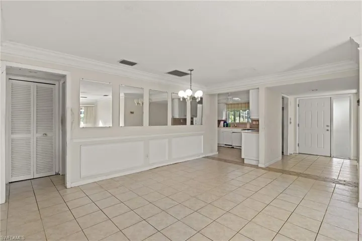 Unfurnished living room featuring ceiling fan with notable chandelier, crown molding, and light tile patterned flooring