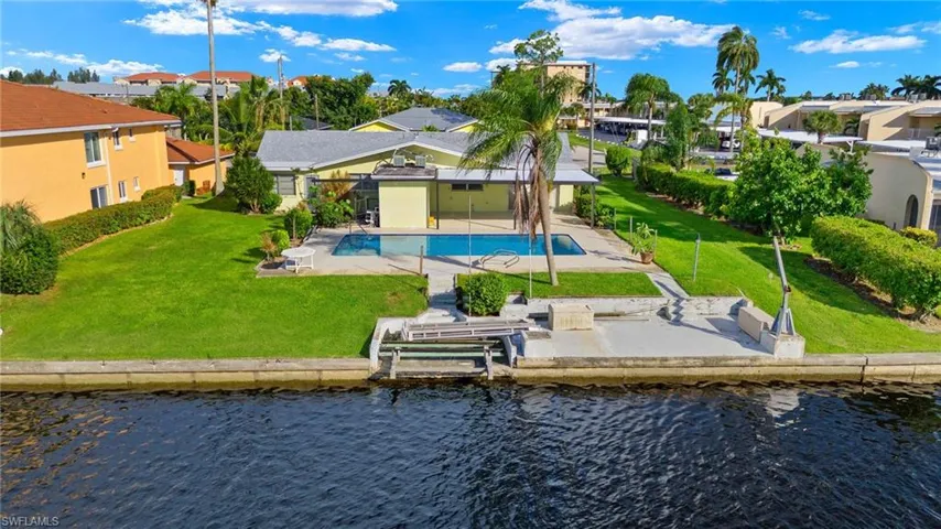 Back of property with a community pool, a lawn, a water view, and a patio
