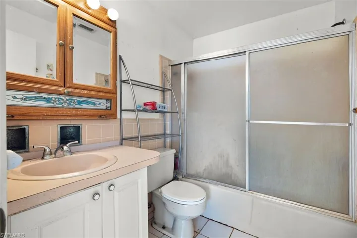 Full bathroom with tile patterned floors, toilet, combined bath / shower with glass door, tasteful backsplash, and vanity