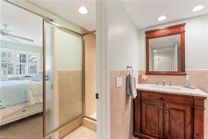 Bathroom featuring ceiling fan, tile patterned flooring, vanity, a shower with shower door, and tile walls
