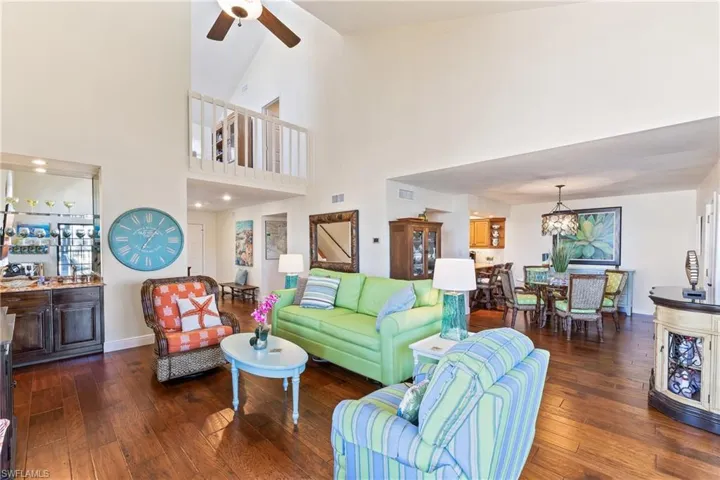 Living room featuring ceiling fan with notable chandelier,  wood flooring, and high vaulted ceiling