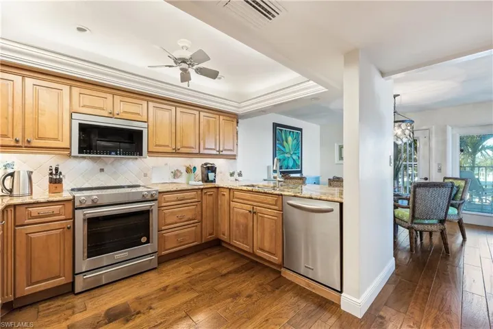 Kitchen with backsplash, a raised ceiling, stainless steel appliances, and beautiful wood flooring