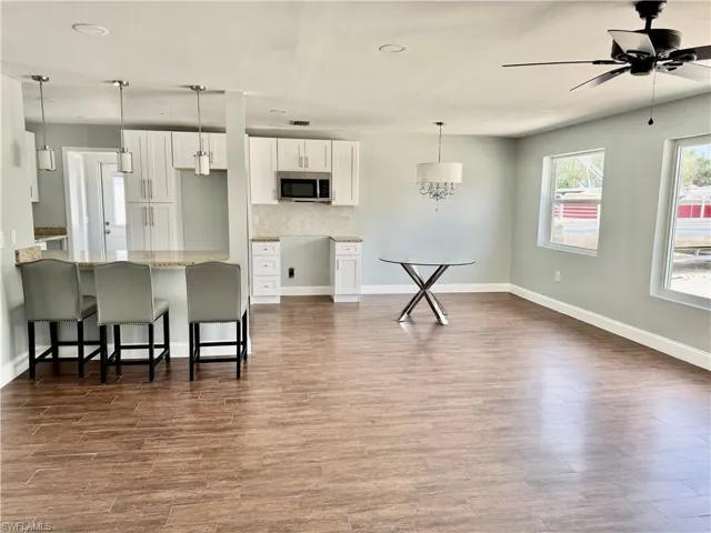 Kitchen featuring white cabinets, a breakfast bar, a peninsula, stainless steel microwave, and light stone counters