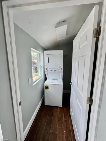 Laundry area featuring dark wood-style flooring, stacked washer / dryer, laundry area, and baseboards