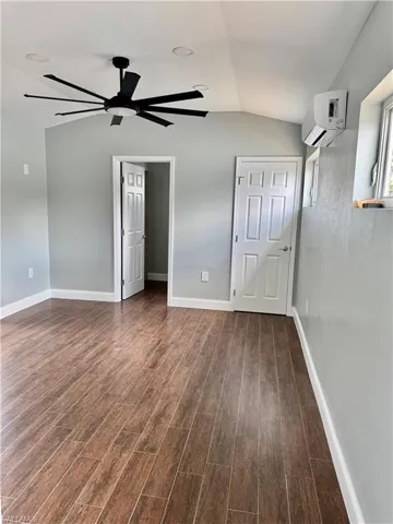 Unfurnished bedroom with baseboards, dark wood-type flooring, vaulted ceiling, and a wall unit AC