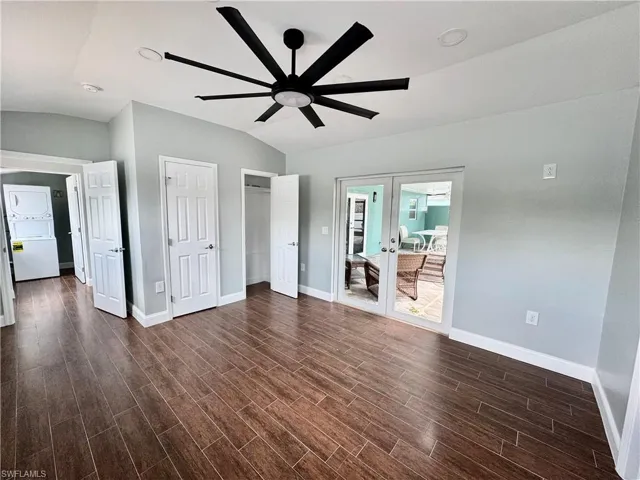 Unfurnished bedroom featuring dark wood-type flooring, baseboards, stacked washer / drying machine, and lofted ceiling