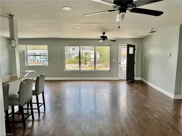 Living room featuring a healthy amount of sunlight, dark wood-style flooring, baseboards, and a ceiling fan
