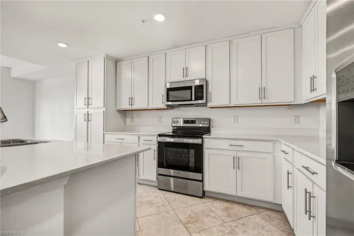 Kitchen with appliances with stainless steel finishes, white cabinets, light stone counters, light tile patterned floors, and recessed lighting