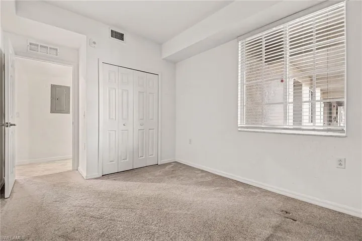 Unfurnished bedroom with light carpet, electric panel, and a closet