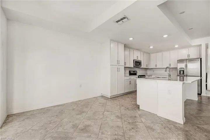 Kitchen featuring white cabinetry, a kitchen island with sink, appliances with stainless steel finishes, recessed lighting, and light stone counters