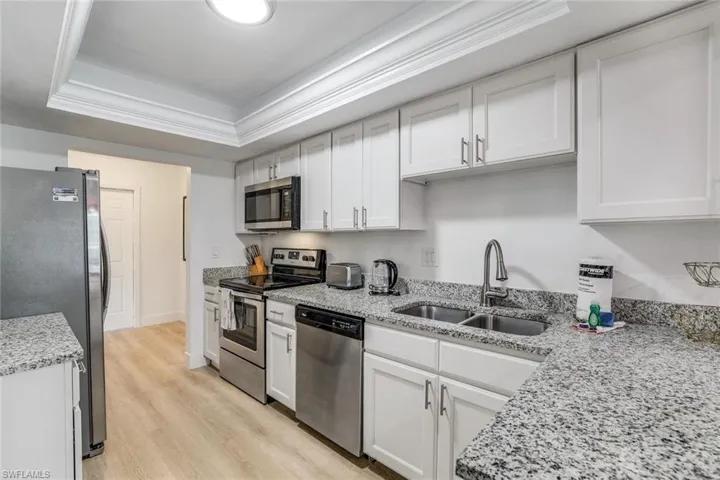 Kitchen with light hardwood / wood-style flooring, a raised ceiling, sink, white cabinets, and appliances with stainless steel finishes