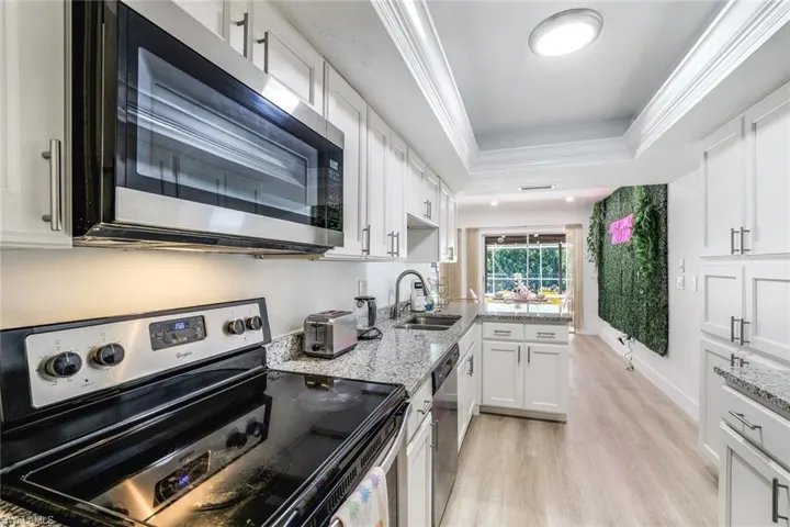 Kitchen with light hardwood / wood-style flooring, stainless steel appliances, a tray ceiling, white cabinets, and sink