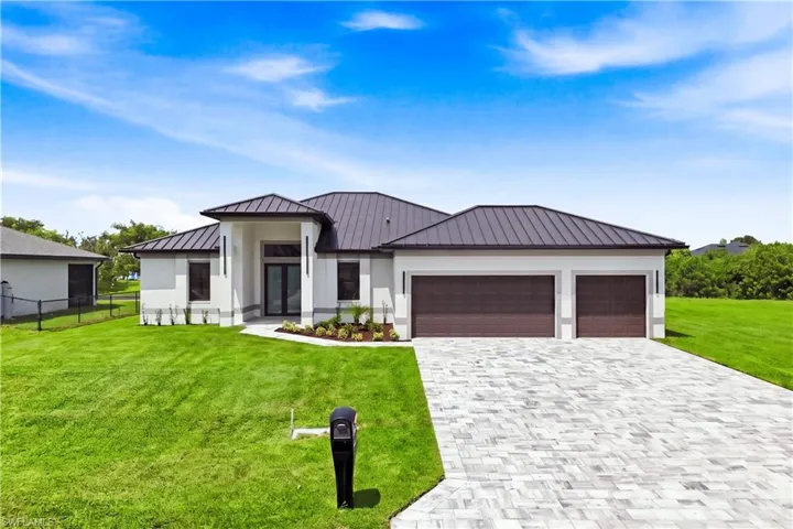 Modern exterior featuring a dark metal roof, dual garage doors, a paver driveway, and a well-maintained lawn