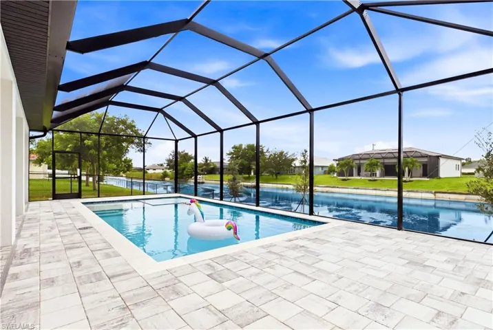 Screened-in outdoor living space featuring a rectangular swimming pool with integrated steps, a spacious paver deck, and direct canal access