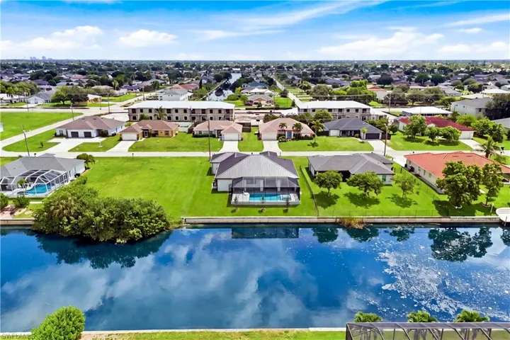 Waterfront property featuring a screened-in pool, direct canal access, and a lush green lawn
