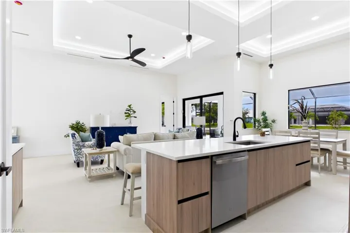 Spacious kitchen island with light wood-finish cabinetry and white countertop, integrated dishwasher, and black fixtures