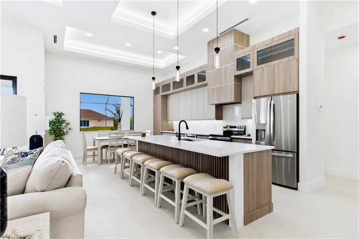 Modern kitchen featuring a large island with white countertop, integrated stainless steel appliances, wood-finish cabinetry, and recessed lighting