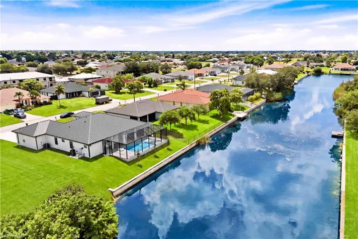 Waterfront property with a screened-in pool enclosure, a private dock, manicured lawn, and a metal roof
