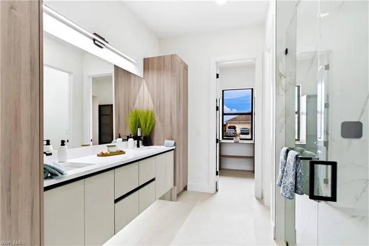 Dual sink vanity with white countertop, extensive wall mirror, wood-finish cabinetry, and glass-enclosed shower