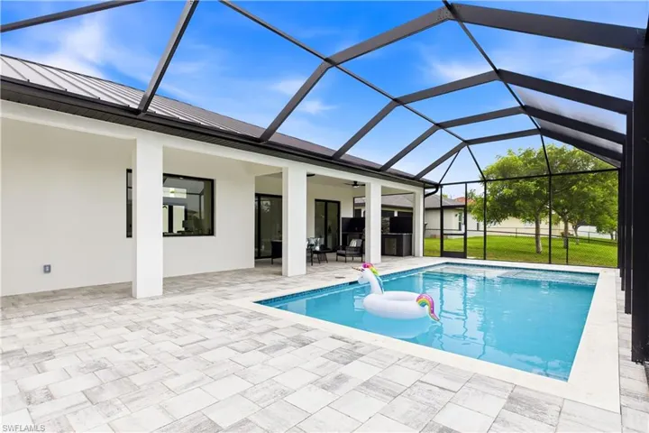 Screen-enclosed pool area featuring a rectangular pool, light-toned paver decking, and a covered lanai with white columns
